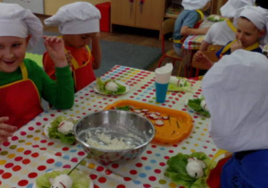 Przedszkolaki siedzące przy stoliku, zadowolone , podziwiają swe wytwory kulinarne.